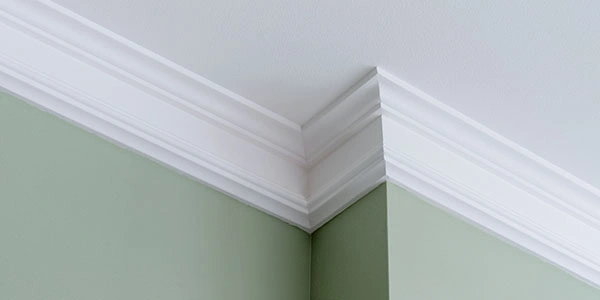 Close-up of a clean crown molding corner against a dark green wall